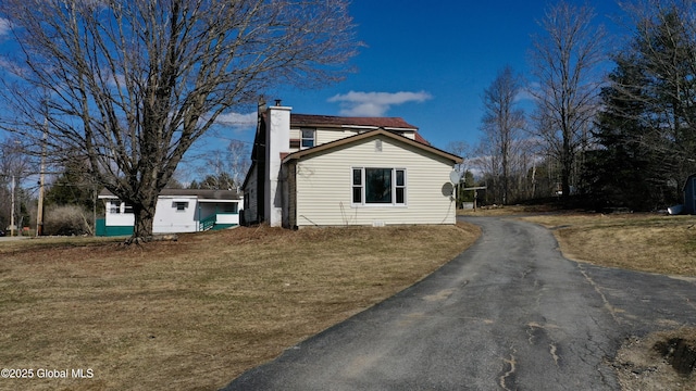 view of side of property featuring a chimney, aphalt driveway, and a lawn
