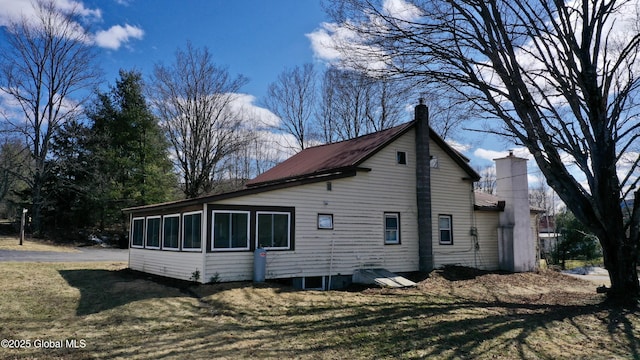 view of side of home featuring a chimney, metal roof, and a lawn