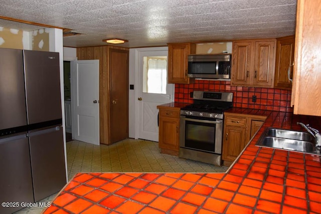 kitchen featuring a sink, brown cabinetry, appliances with stainless steel finishes, and tile countertops