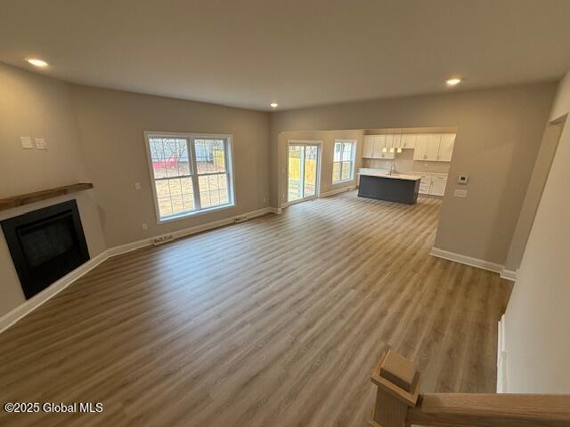unfurnished living room with recessed lighting, a fireplace, baseboards, and wood finished floors