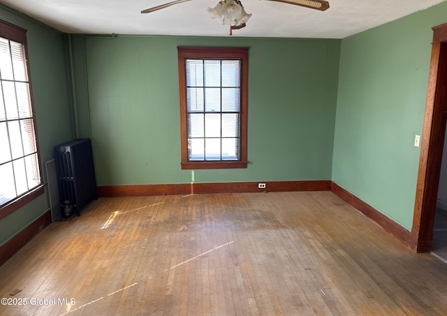 empty room featuring hardwood / wood-style flooring, baseboards, a ceiling fan, and radiator