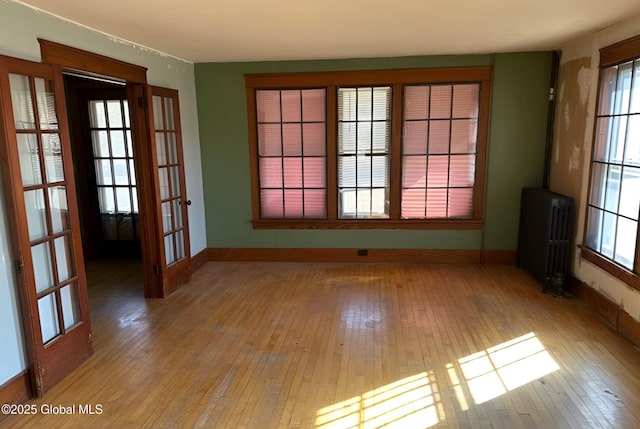 spare room with baseboards, radiator heating unit, hardwood / wood-style floors, and a healthy amount of sunlight