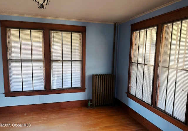 unfurnished room featuring radiator heating unit, ornamental molding, baseboards, and wood finished floors