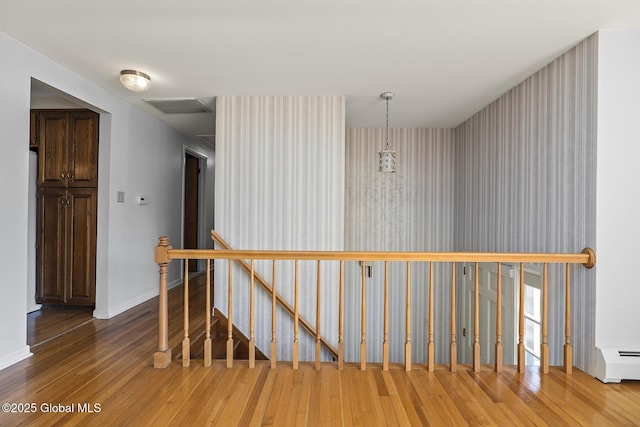 corridor featuring hardwood / wood-style floors, baseboard heating, an upstairs landing, baseboards, and visible vents