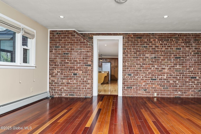 spare room featuring wood-type flooring, a baseboard heating unit, recessed lighting, and brick wall