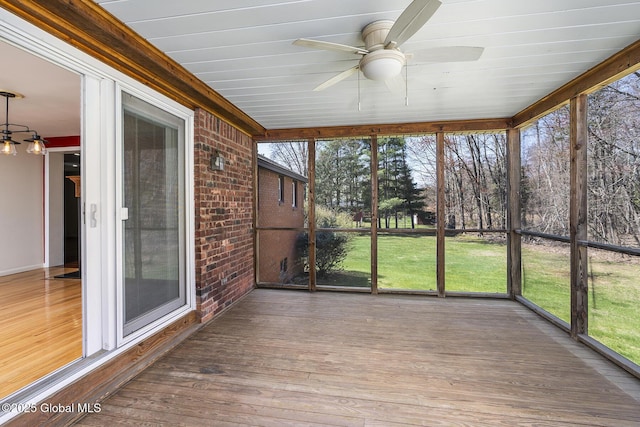 unfurnished sunroom with a deck, a ceiling fan, and brick wall