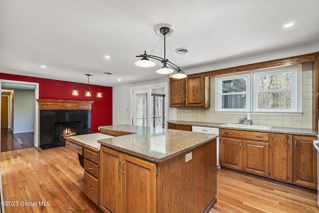 kitchen featuring tasteful backsplash, a sink, a lit fireplace, a center island, and light wood-type flooring