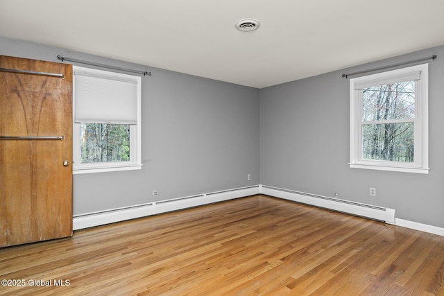 spare room featuring visible vents, wood finished floors, plenty of natural light, and a baseboard radiator