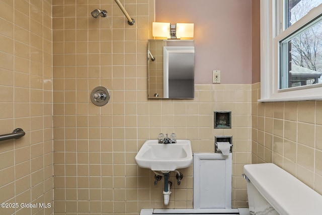 bathroom with tile walls, toilet, walk in shower, and a sink