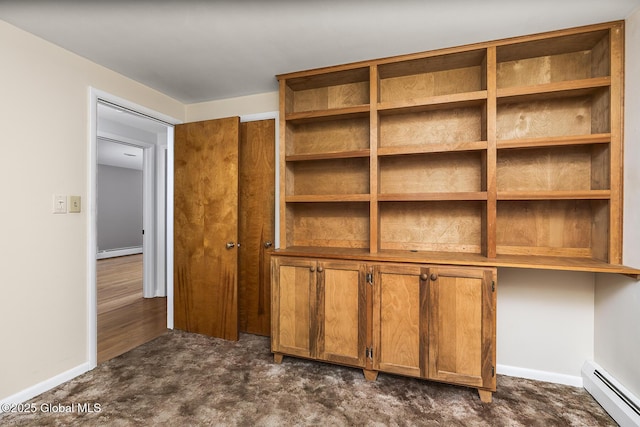 unfurnished bedroom featuring dark colored carpet, a baseboard heating unit, and baseboards