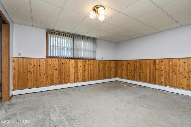 empty room featuring wainscoting, wooden walls, carpet flooring, and a drop ceiling