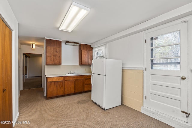 kitchen featuring brown cabinets, a sink, light countertops, freestanding refrigerator, and light colored carpet