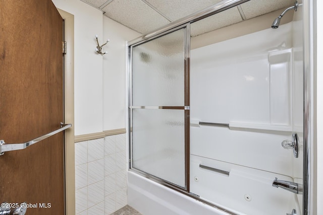 bathroom featuring tile walls, shower / bath combination with glass door, and a drop ceiling