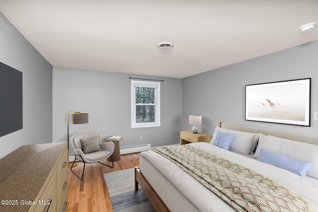 bedroom with baseboard heating, visible vents, wood finished floors, and baseboards