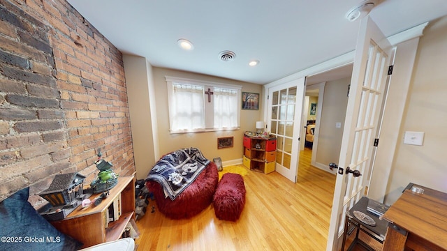 living area with visible vents, wood finished floors, french doors, brick wall, and baseboards