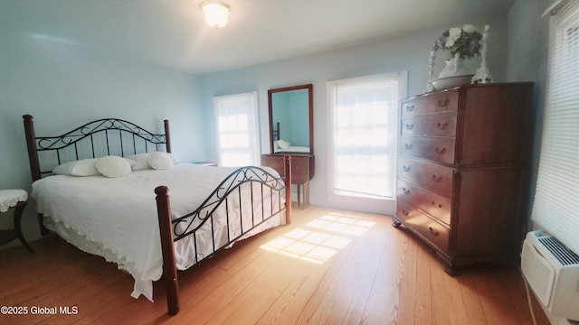 bedroom with light wood-style flooring, multiple windows, and a wall mounted AC