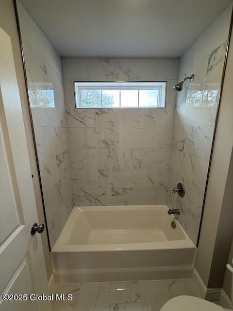 full bath featuring toilet, marble finish floor, baseboards, and washtub / shower combination