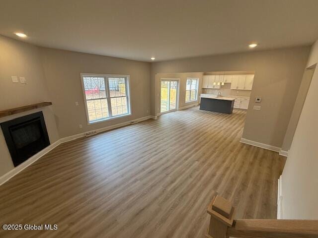 unfurnished living room with recessed lighting, a fireplace, baseboards, and wood finished floors
