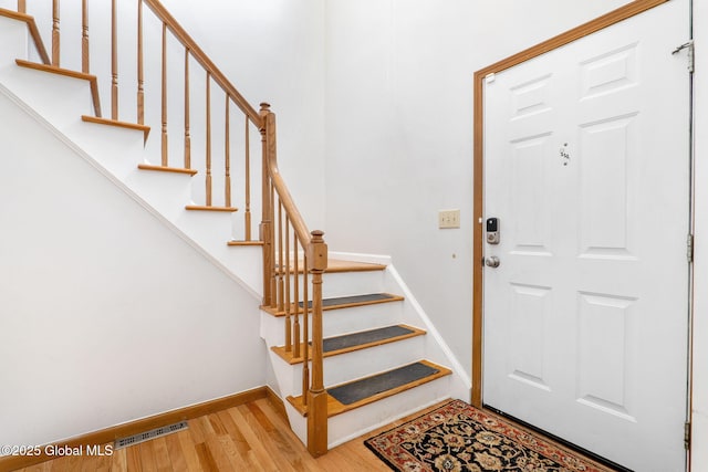 foyer with stairway, baseboards, wood finished floors, and visible vents