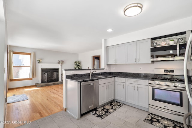 kitchen with appliances with stainless steel finishes, a sink, a peninsula, a glass covered fireplace, and dark stone counters