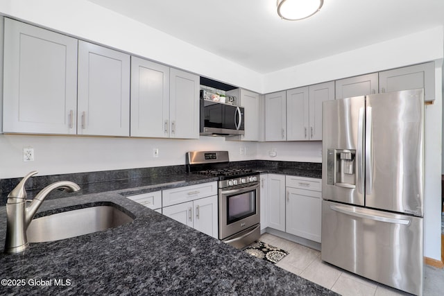 kitchen featuring a sink, light tile patterned floors, stainless steel appliances, and dark stone countertops