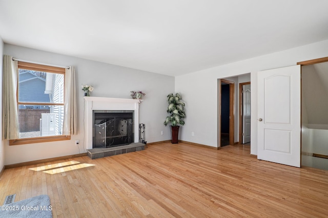 unfurnished living room featuring a fireplace with raised hearth, baseboards, visible vents, and wood finished floors
