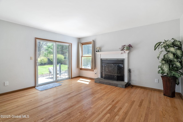 unfurnished living room with light wood-style floors, baseboards, and a glass covered fireplace