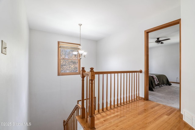 stairs featuring baseboards, ceiling fan with notable chandelier, wood finished floors, and visible vents