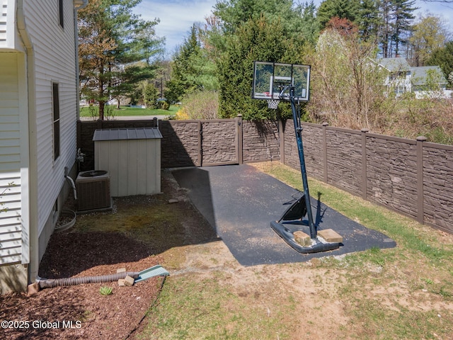 view of basketball court featuring a fenced backyard and a storage unit