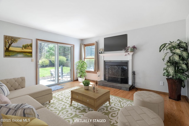 living area featuring baseboards, a glass covered fireplace, and light wood finished floors