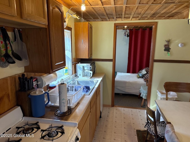 kitchen with a sink, brown cabinets, light floors, light countertops, and white range with gas stovetop
