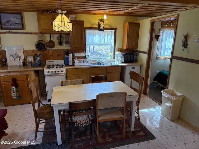 kitchen with light floors, light countertops, a sink, white appliances, and pendant lighting