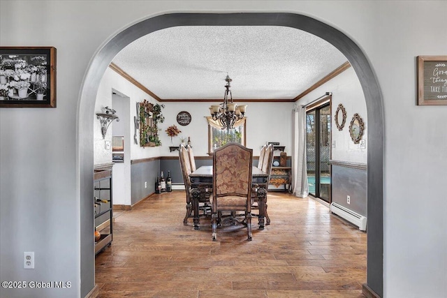 dining room featuring arched walkways, a textured ceiling, a baseboard radiator, and crown molding