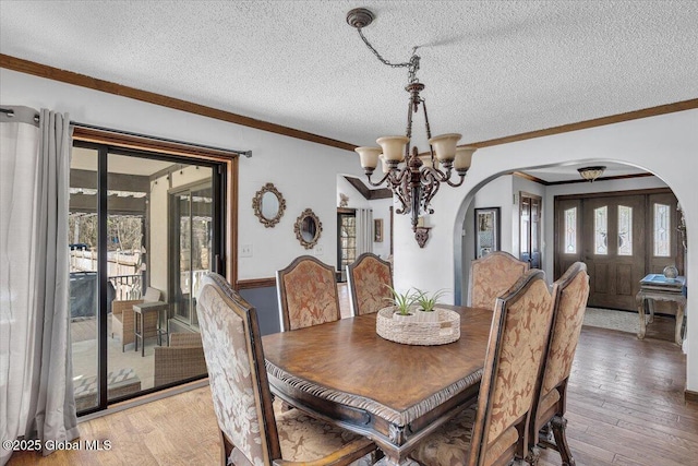 dining space featuring a textured ceiling, light wood-style flooring, arched walkways, and a notable chandelier