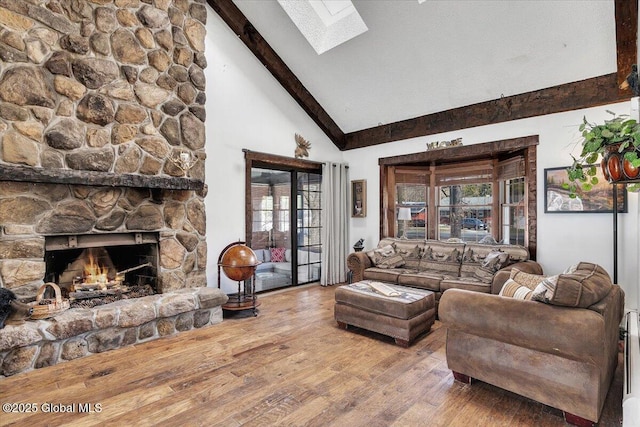 living area with high vaulted ceiling, a skylight, beamed ceiling, a fireplace, and wood-type flooring