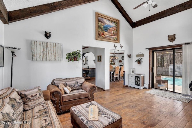 living room featuring high vaulted ceiling, a ceiling fan, wood finished floors, arched walkways, and beamed ceiling