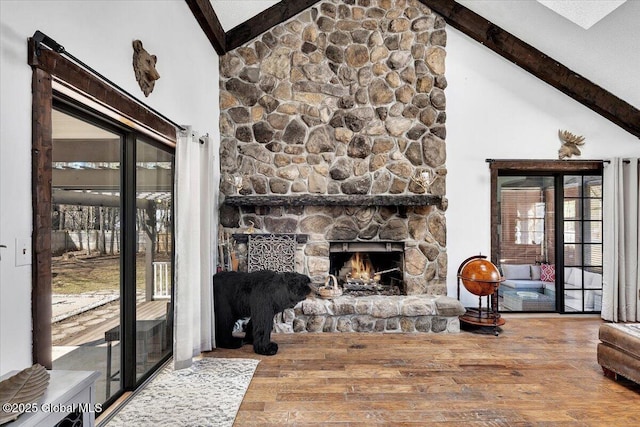 living room with wood finished floors, beam ceiling, high vaulted ceiling, and a stone fireplace