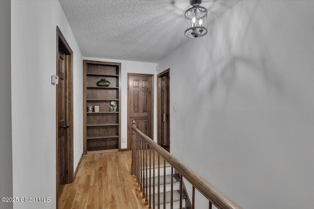hall with an upstairs landing, built in features, a textured ceiling, and light wood-style flooring