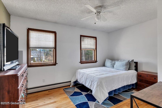 bedroom featuring a baseboard heating unit, wood finished floors, a textured ceiling, and multiple windows