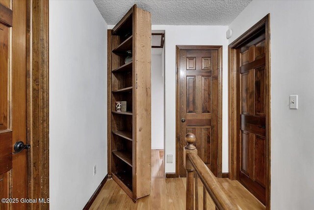 corridor with light wood-style flooring, baseboards, and a textured ceiling