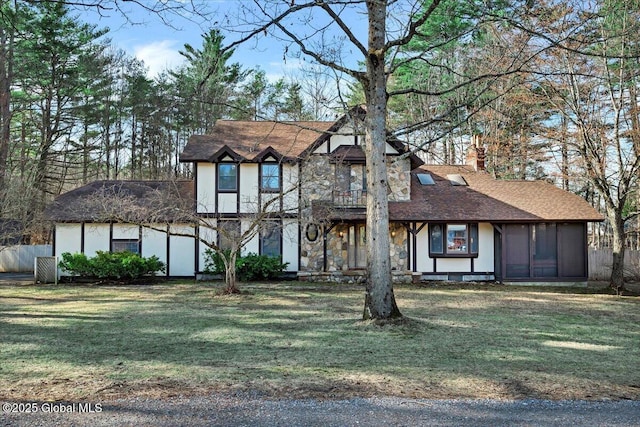 tudor home with a chimney, a front lawn, roof with shingles, and a sunroom