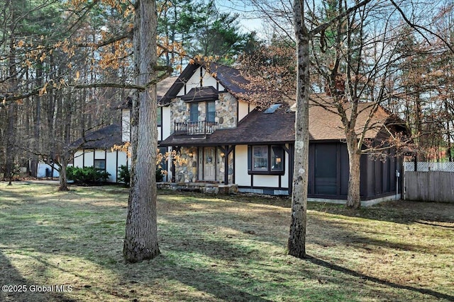 view of front of house featuring a shingled roof, a front lawn, a balcony, and fence