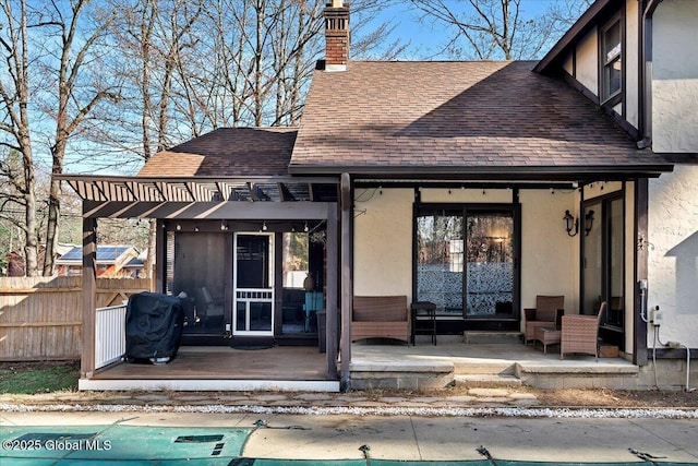 property entrance featuring stucco siding, fence, a chimney, and a shingled roof
