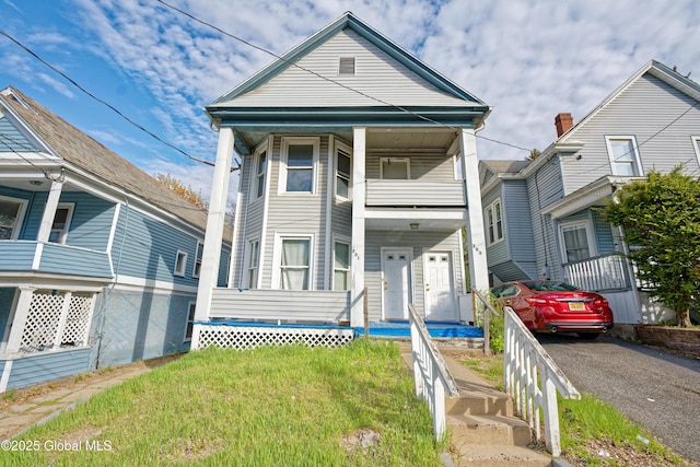 view of front of house featuring covered porch, a balcony, and a front lawn