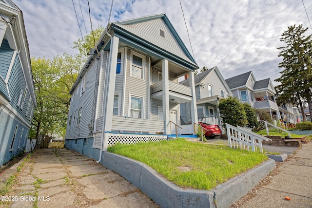greek revival house featuring a porch, a front yard, a balcony, and a residential view