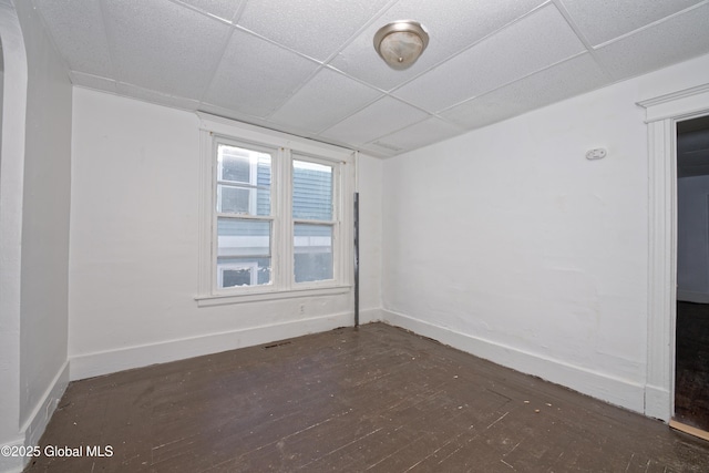 unfurnished room featuring baseboards, a drop ceiling, and wood finished floors