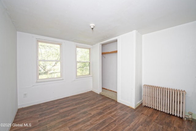 unfurnished bedroom featuring baseboards, wood finished floors, radiator, and a closet