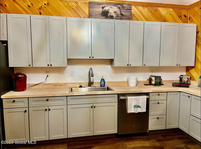kitchen with dark wood-style flooring, wooden walls, light countertops, dishwasher, and a sink