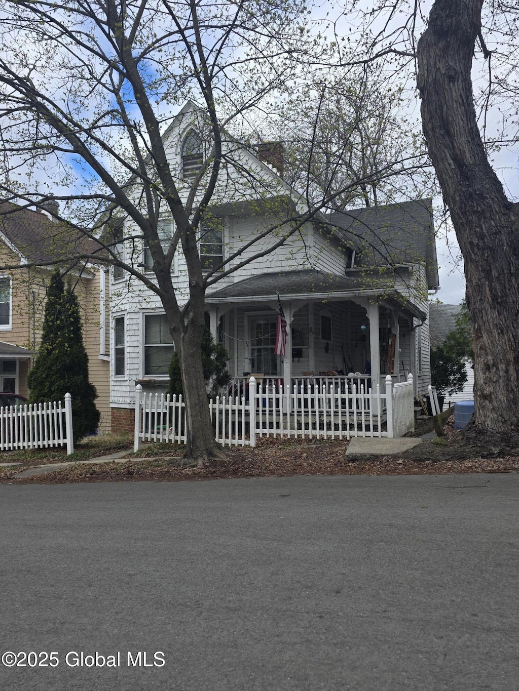 view of front facade featuring a chimney, covered porch, and fence