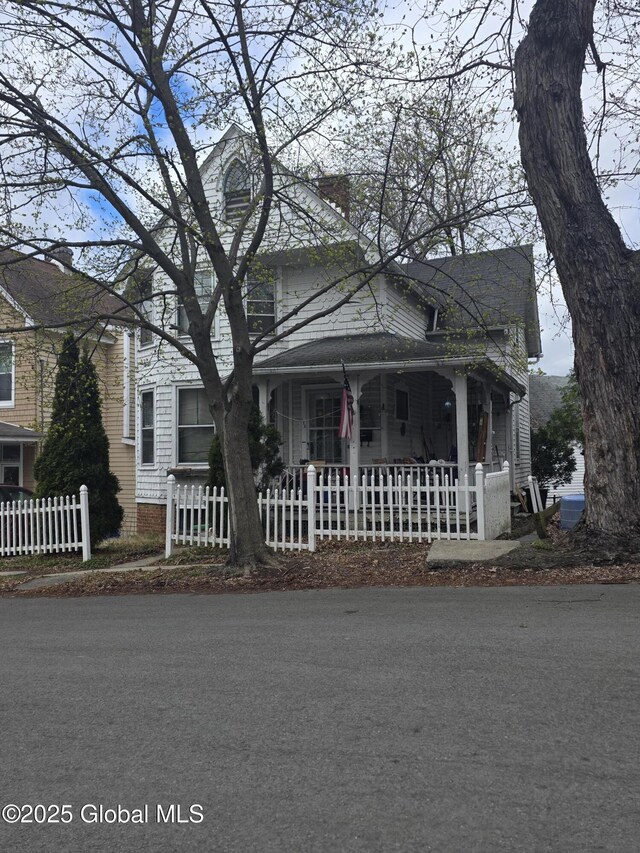 view of front facade featuring a chimney, covered porch, and fence